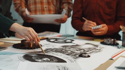 A diverse team collaborates on an engineering design, sketching detailed plans and illustrations on a table filled with tools and project papers in a professional workspace. SACTR