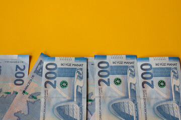 Close-up view of multiple 200 Azerbaijani manat banknotes arranged neatly against a vibrant yellow background, showcasing modern design and national currency details in a financial context.
