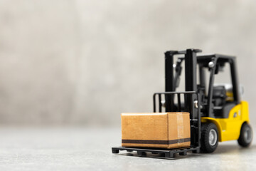 Yellow forklift on bright textured background. Logistics concept. Logistics and supply chain management for online shopping concept. Delivery of goods or products to the store worldwide. Cardboard box