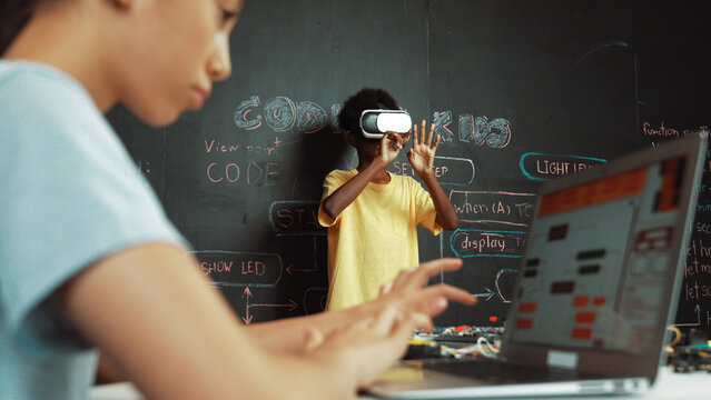 Closeup of school girl hand coding program while african student using VR interact with metaworld. Smart boy wearing virtual reality glasses and playing video games at innovative class. Edification.