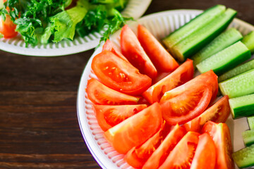 Close-up of fresh cucumber and tomato salad on a white plate placed on a natural wooden table, with focus on vibrant colors and texture of the vegetables.


