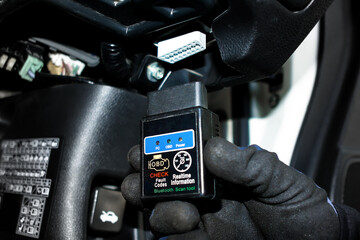 OBD2 Scanner Tool, A gloved hand holds an OBD2 scanner, ready to connect to a car's diagnostic port for checking fault codes and real time information. Car diagnostics, auto repair tool.