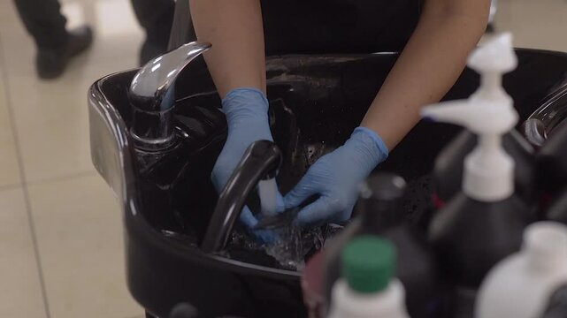 hairdresser wearing gloves washing comb in sink in hair salon.