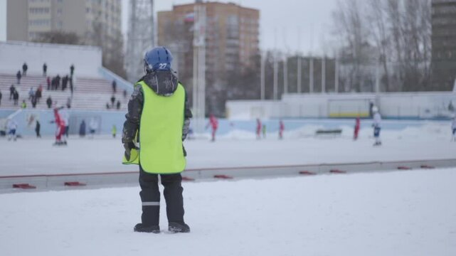 Boy service watches bandy game at stadium.