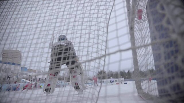 A bandy goalie stands in the goal with a stadium in the background.