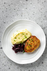 delicious plate featuring golden-brown chicken cutlet served with creamy mashed potatoes and side of roasted beets, garnished with fresh herbs, all on a modern white plate against a light background.