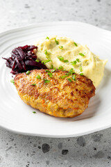 delicious plate featuring golden-brown chicken cutlet served with creamy mashed potatoes and side of roasted beets, garnished with fresh herbs, all on a modern white plate against a light background.