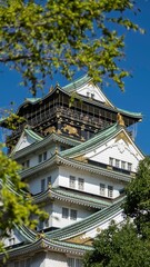 Osaka Castle framed by green leaves.