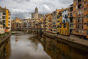 Obraz premium The Onyar River runs through Girona's historic center. The facades of the buildings along the river are painted in warm tones such as yellow, orange, red, and white. Spain