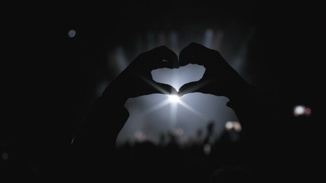 Light music show. Close-up shot. Dark silhouette of female hands in the shape of heart fingers, backlight from the stage 