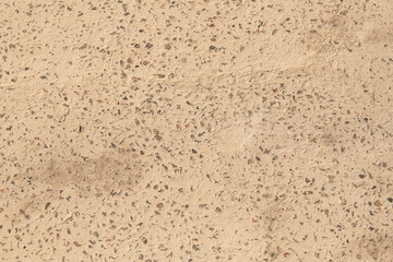 A close-up view reveals a textured surface composed of natural aggregates, showcasing earthy tones under bright sunlight. The patterns and colors create an inviting atmosphere