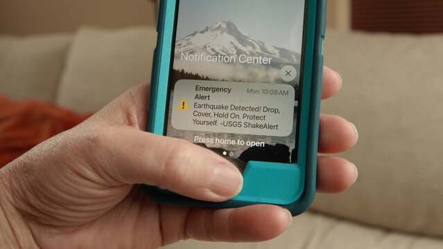 Close up of a hand holding a phone with an emergency earthquake alert displayed on screen