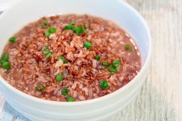 Close up of a bowl of brown rice porridge with chopped green onions on a white wooden surface, Healthy comfort food.