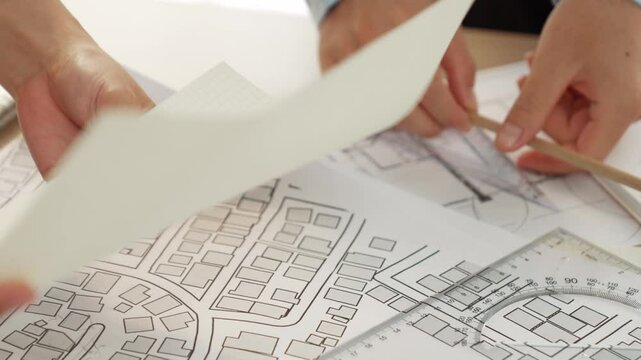 Smart architect and safety engineer discussion about building blueprint on table with architectural document, measurement tools and wooden block scatter around at modern office. Closeup. Delineation.