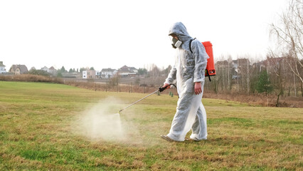 Man wearing protective suit treats the lawn from insect parasites using poison sprayer. Weedkiller. Gardener in a full face mask respirator with personal protective equipment. High quality photo.