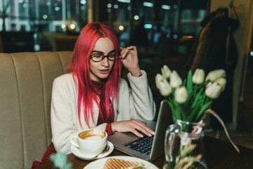 A woman with red hair is sitting with a laptop in a cafe