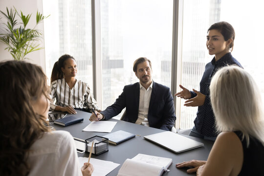 Speaking on conference. Confident young Indian woman team leader executive present project idea of sales grows at round table meeting of teammates stakeholders consulting colleagues propose solution