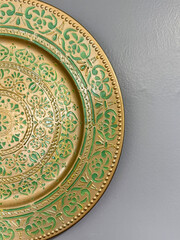 Decorative green and gold embossed plate on gray wall