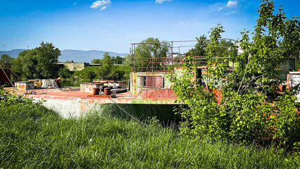 Old Rusty Barge Docked on Riverbank with Green Grass and Trees