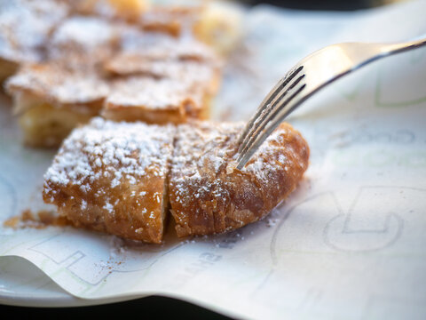 Closeup of hands eating traditional Greek bougatsa, a sweet cream pie pastry with filo dough, dusted with powdered sugar and cinnamon. Popular breakfast or snack from Thessaloniki and Serres, Greece.