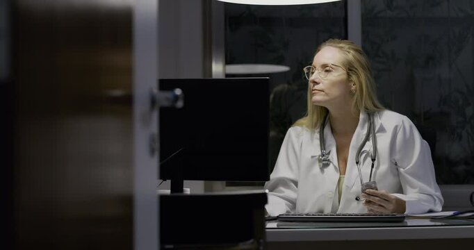 Female doctor working late at computer in medical office at night, typing on keyboard, focused and concentrated, professional healthcare environment