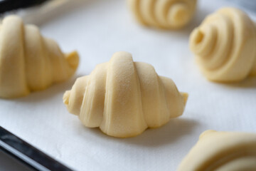 Close up of layered of several fluffy leavened uncooked traditional French croissants dough in a baking tray over paper sheet before put in oven. 
