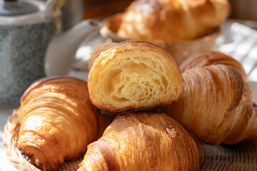 A cooked traditional French butter croissants cut to show an internal  fluffy of multiple layers. With teapot and cup in background. It's a buttery, flaky pastry fold with butter in multiple layers.