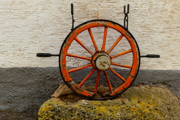 Colorful vintage wheel displayed on a stone against a textured wall in a quaint outdoor setting