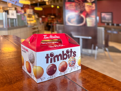 Calgary, Alberta, Canada. Apr 20, 2025. A box of Tim Hortons Timbits sits on a wooden table inside a Tim Hortons restaurant, ready to be enjoyed as a treat.