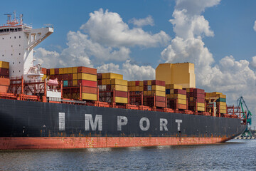Large container ship loaded with multicolored cargo containers, docked at a port with the word...