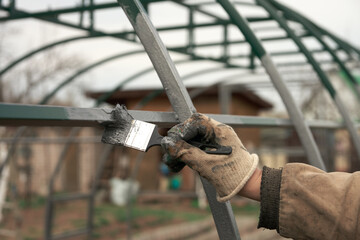 Anticorrosive coating of the metal structure. A man's hand is painting the frame of a greenhouse...