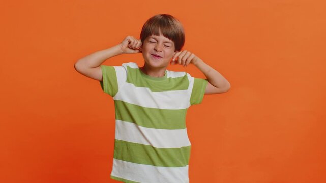 Cheerful funny bully young cute boy showing tongue making faces at camera, fooling around, joking, aping with silly face, teasing. Preteen child kid 6 years old on orange background. Little children