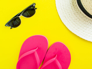 Flatlay, summer vacation. Straw hat, sunglasses and flip flops on a yellow background.