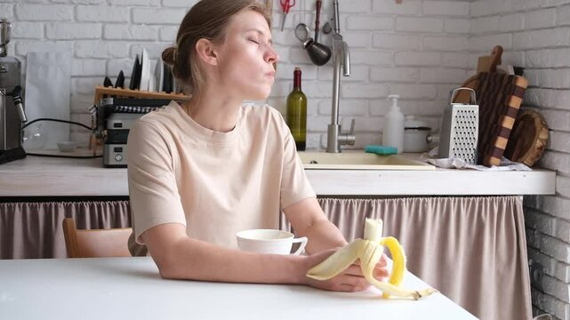 young woman eating banana and drinking coffee in the morning in the kitchen , daily morning routines, talking to her dog