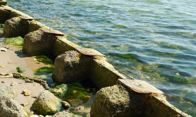 Series of weathered concrete blocks, showing signs of decay and algae growth, extend into the sea...