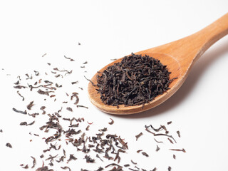 close-up of a wooden spoon with black than on a white background. Tea leaves are scattered around