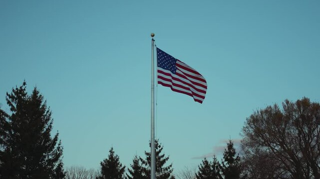 American flag waving at sunset with blue sky. Golden sunlight highlights the stars and stripes. Symbol of freedom, pride, and patriotism in the USA