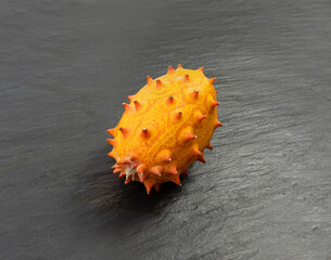 Kiwano on black plate, jelly melon, cucumis metuliferus ripe fruit, orange spiked horned melon