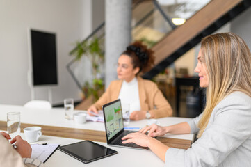Businesswoman analyzing financial data and performance over laptop while working together in board room