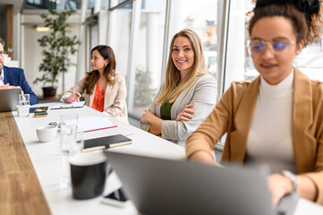 Confident female professional with arms crossed smiling at camera while working with coworkers in board room
