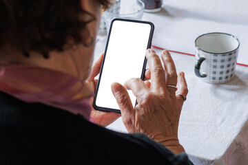 Elderly woman using smartphone while seated at dining table during casual gathering at home