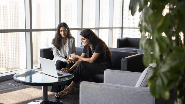 Two women workmates discuss ideas or strategies shown on laptop, analyzing data or financial report, brainstorming creative solutions related on joint task completion, review new business tool, or app