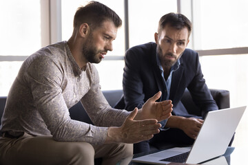 Two businessmen take part in discussion, sit in modern office or meeting room with laptop,...
