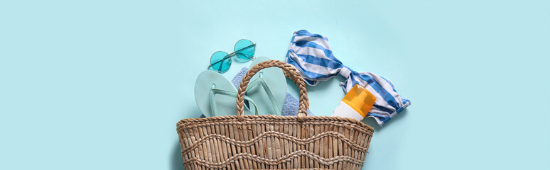 Wicker bag with sunglasses, sunscreen, flip-flops and swimsuit on blue background