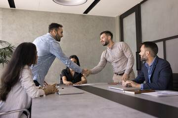 Two young businessmen shaking hands, gesture of agreement, collaboration, or closing of deal, start or finish formal meeting, negotiations process between business parties, smile, expressing respect