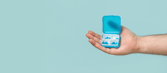 Man's hand holding container with pills on light blue background with space for text