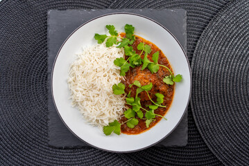 Chicken tikka masala served with basmati rice and coriander garnish on a white plate, placed on a black slate, which sits on a black placemat, creating a visually appealing culinary scene
