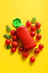 Bottle of ketchup and tomatoes on yellow background