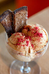 Borodino rye bread crisps topping scoops of rich brown ice cream, delicately sprinkled with vibrant freeze dried raspberry powder, create an enticing dessert presentation in a glass on the table