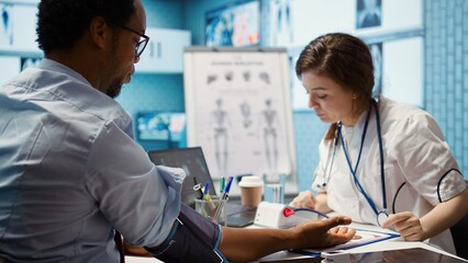 Obraz premium Female medic measuring blood pressure and pulse for a patient, working with blood pressure monitor and other diagnostic tools. Professional cardiology examination, high quality readings. Camera B.